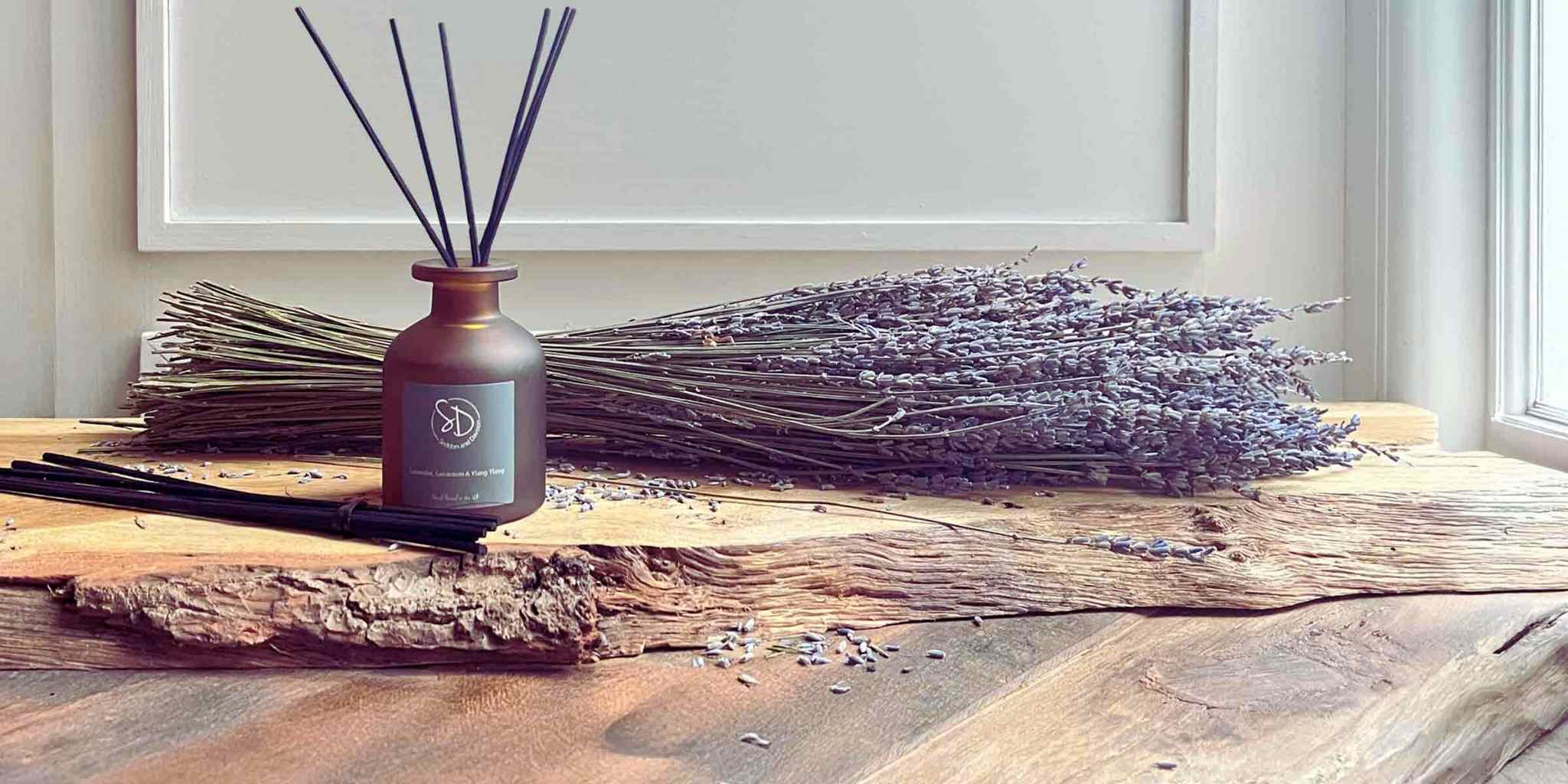 Seddon and Davison Reed Diffuser - Lavender, ylang, ylang and geranium - placed on wooden plank on rustic table with lavender.