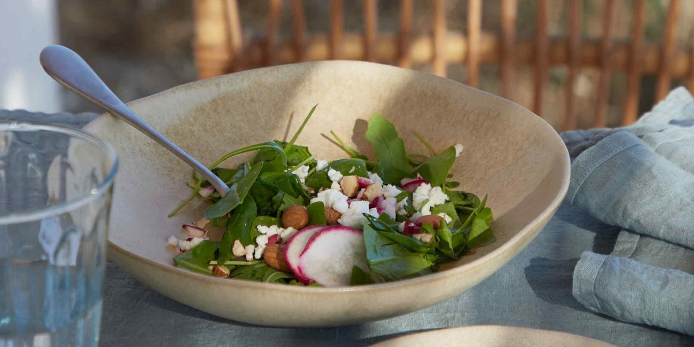 Sand-glazed stoneware salad bowl with salad as part of a Mediterranean-inspired summer table setting