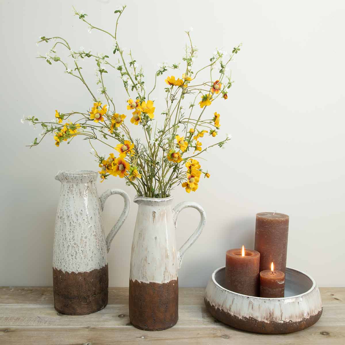Large and small terracotta jugs with matching bowl styled with faux yellow flowers and brown candles