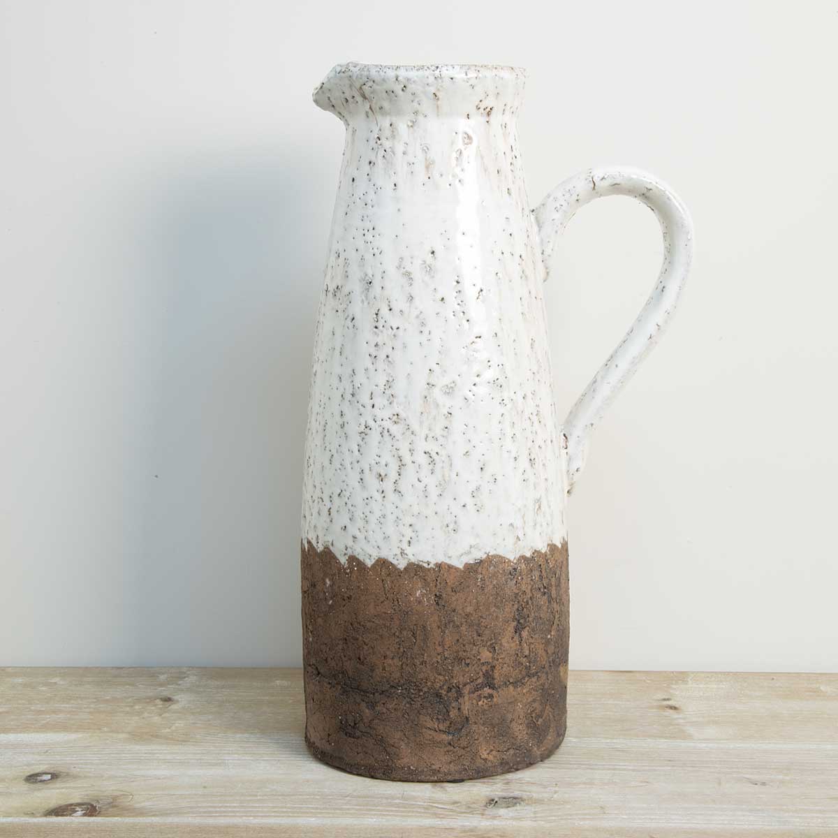 Tall aged ceramic jug with cream glaze and brown base on wooden surface