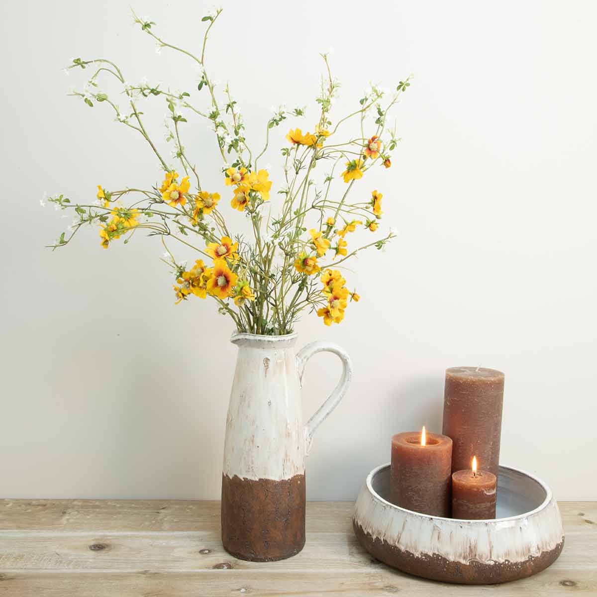 Matching aged terracotta jug and bowl styled with brown pillar candles and faux florals