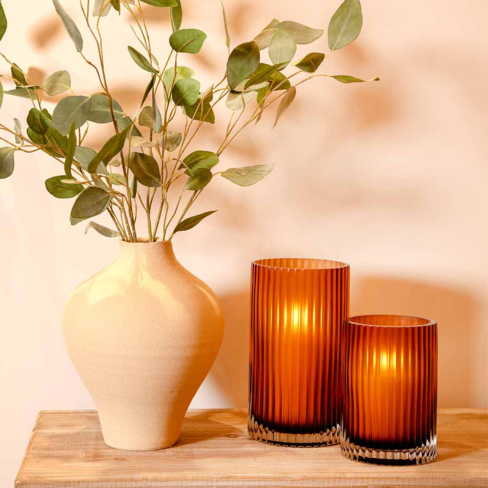 Vase with green leaves and Amber Smoke Fluted Glass Vases on a wooden console