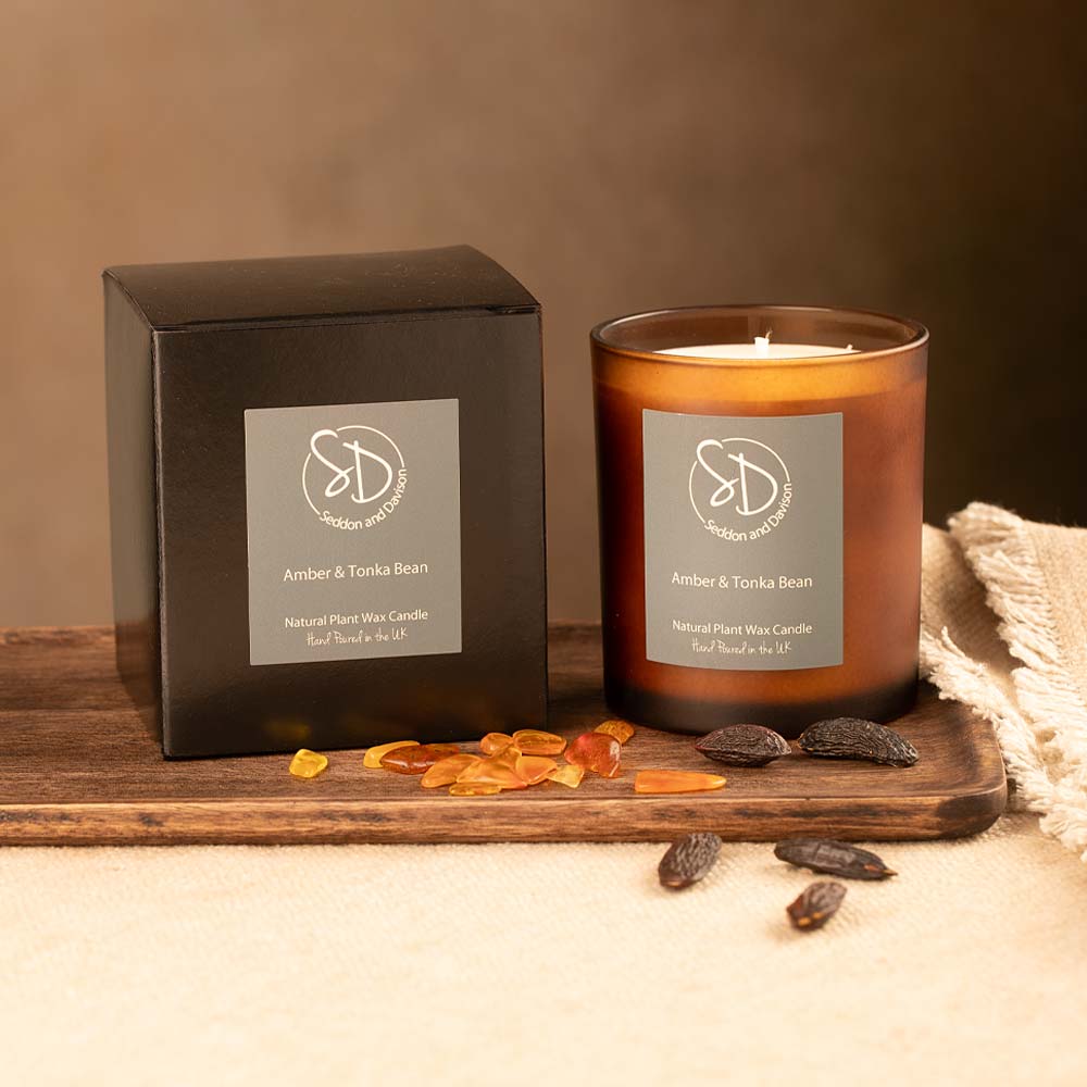 Candle and packaging with 'Amber & Tonka Bean' label on a wooden surface.