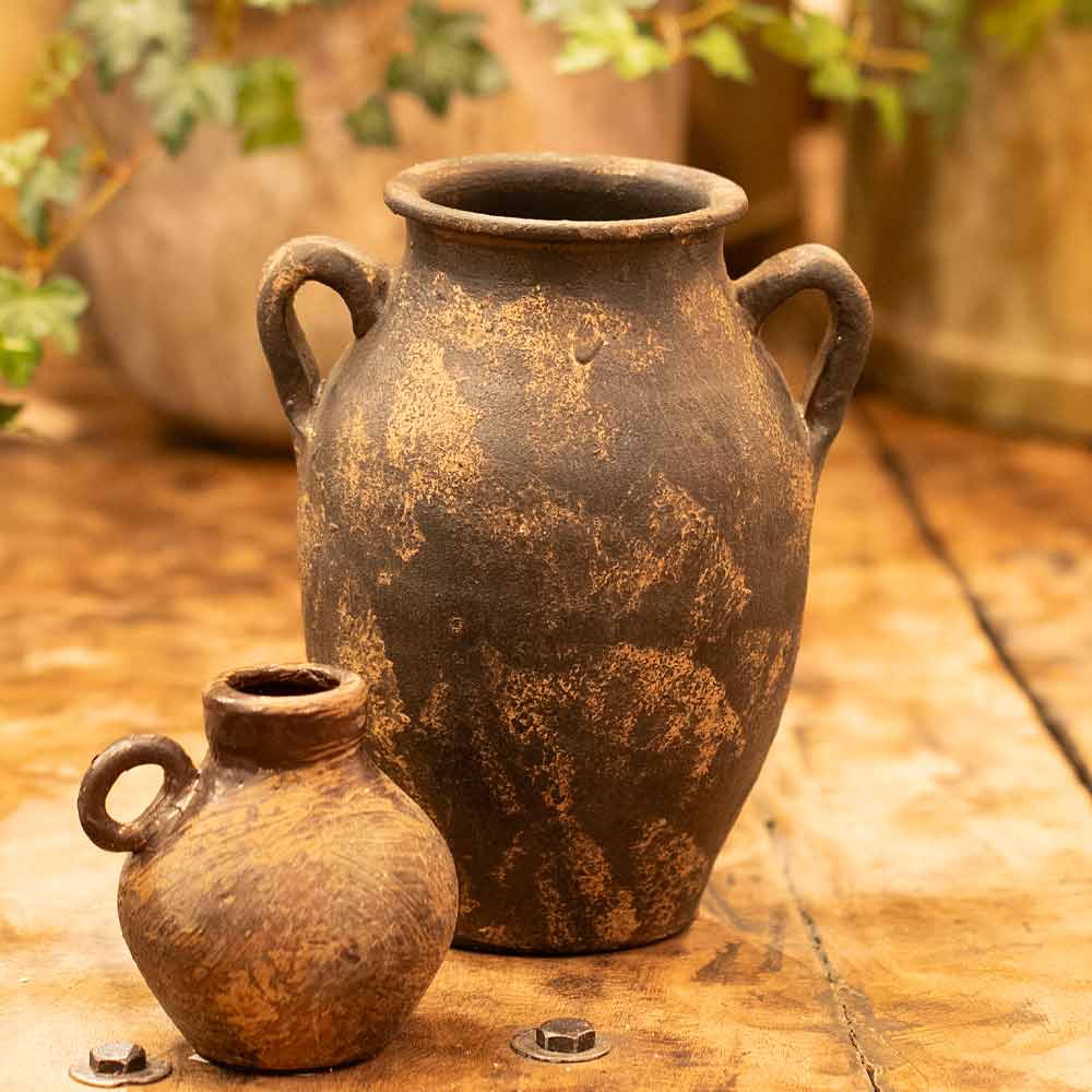Two rustic clay pots, including the Vintage-style Annchi Brown Terracotta Vase on a wooden surface with plants in the background