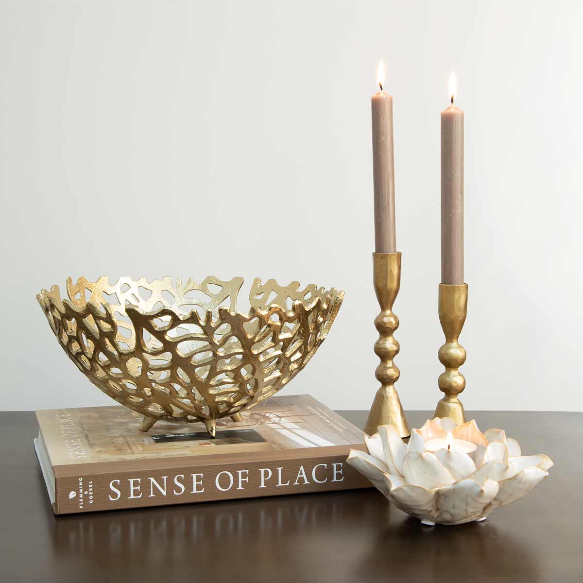 Antique gold coral-effect bowl styled on a coffee table beside brass candlesticks and a flower tealight holder