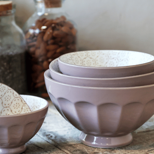 Set of 5 Ares Bowls in taupe with a soft matte finish and delicate patterned interior, stacked on a rustic wooden surface with pantry jars in the background.
