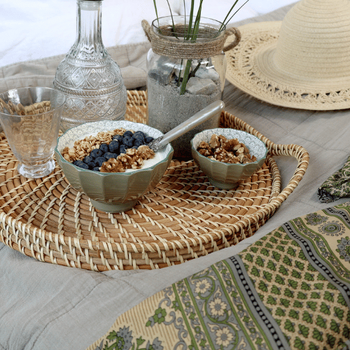 Ares Bowls in Verte - Set of 5. Two bowls from the set displayed with muesli and blueberries on a rattan tray with water and a sun hat.