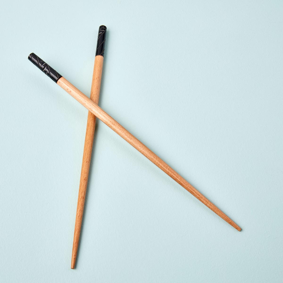 A pair of handcrafted wooden chopsticks with a natural wood finish and black-detailed handles, elegantly displayed on a soft pastel background.