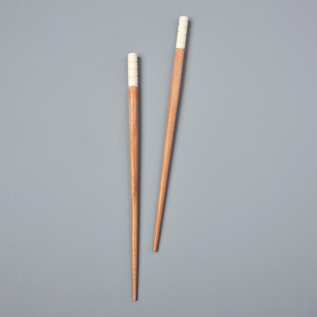 A pair of handcrafted wooden chopsticks with a natural wood finish and hand-wrapped white detailing, elegantly displayed on a soft grey background.