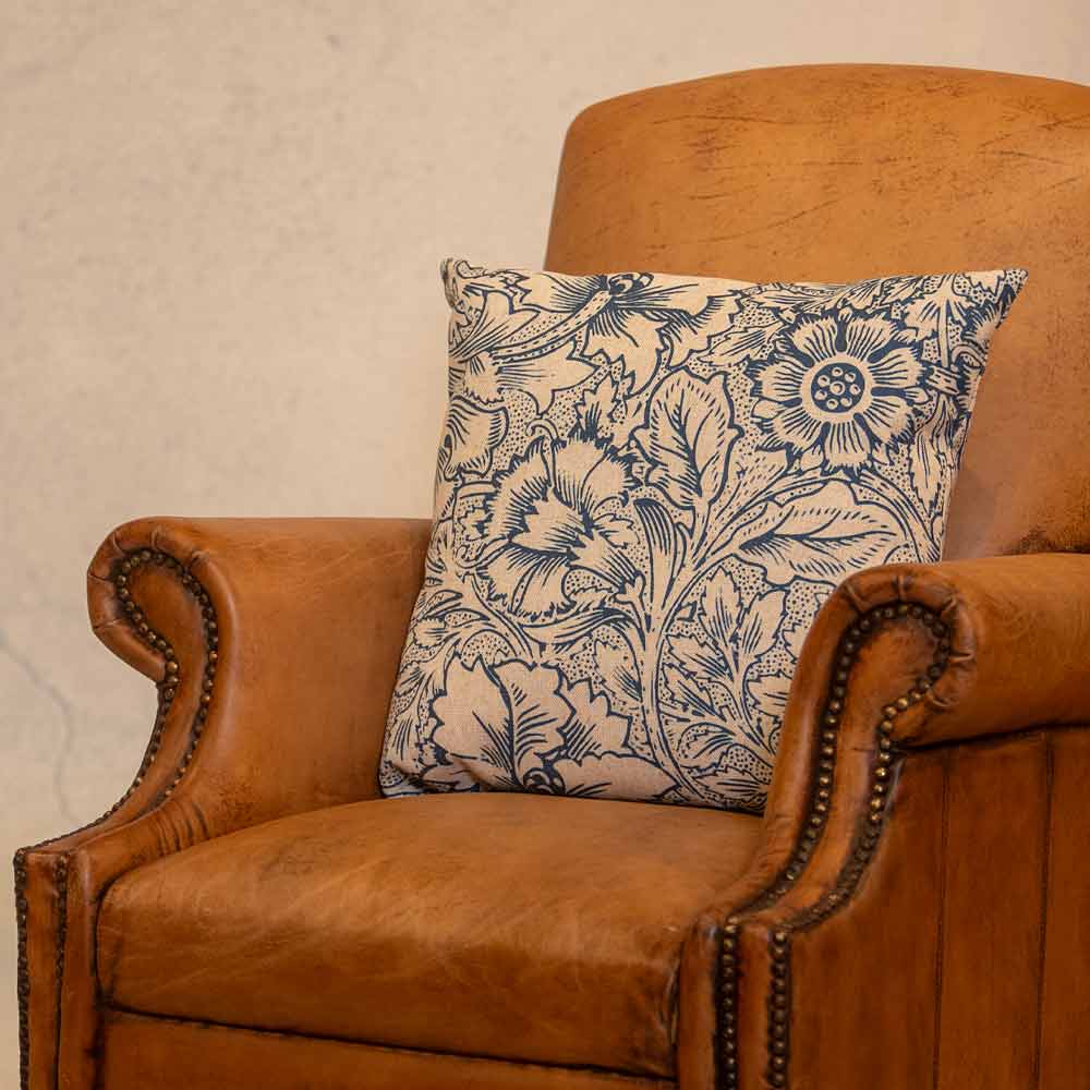 Brown leather armchair with a decorative floral pillow against a beige wall.