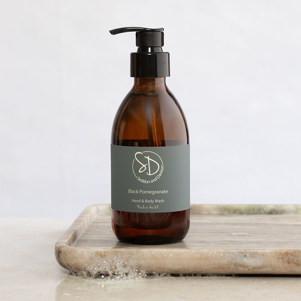 Amber glass pump bottle of Seddon and Davison Black Pomegranate Hand & Body Wash, resting on a light marble tray against a clean white background.