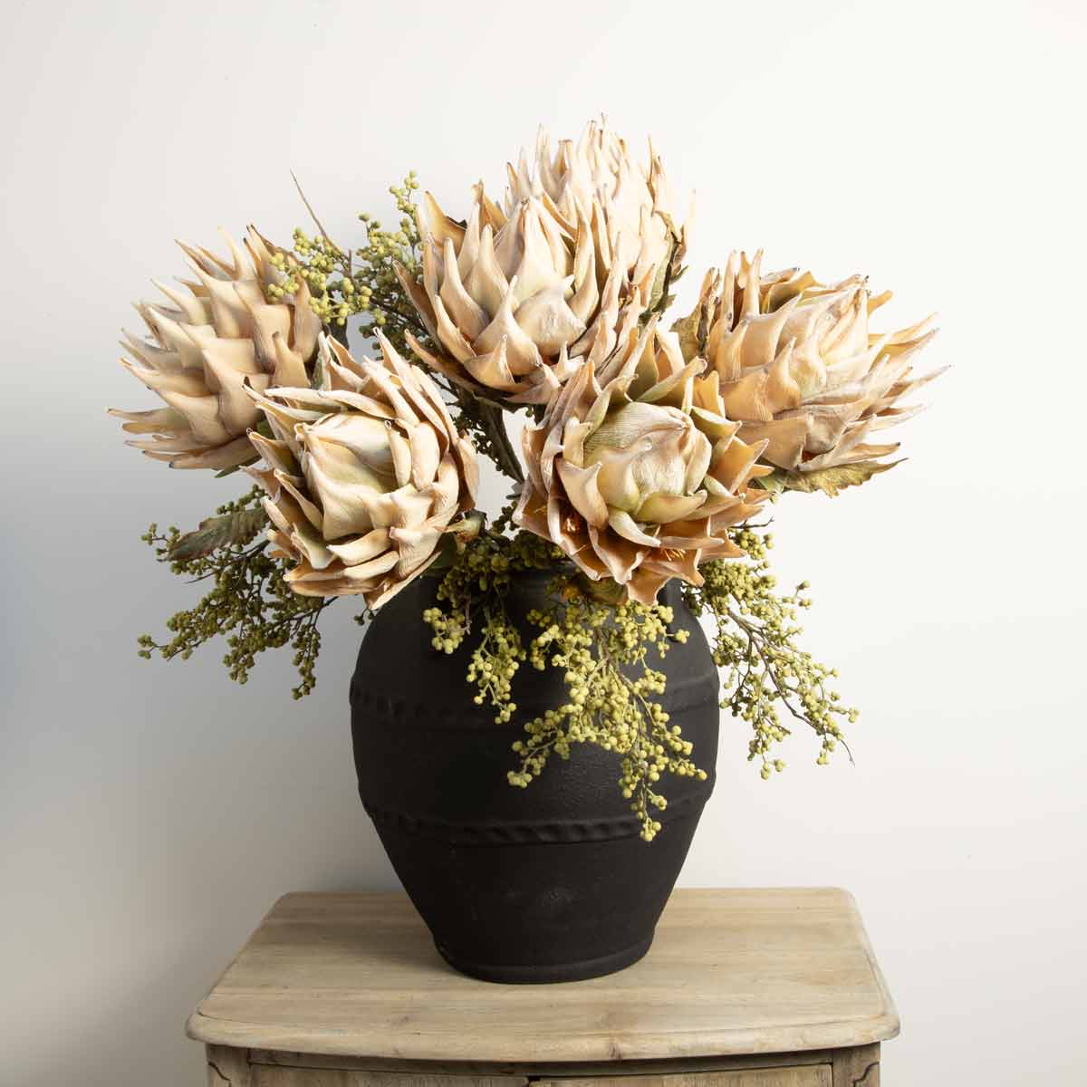 Black terracotta urn vase styled with dried protea flowers and foliage on a rustic wooden side table