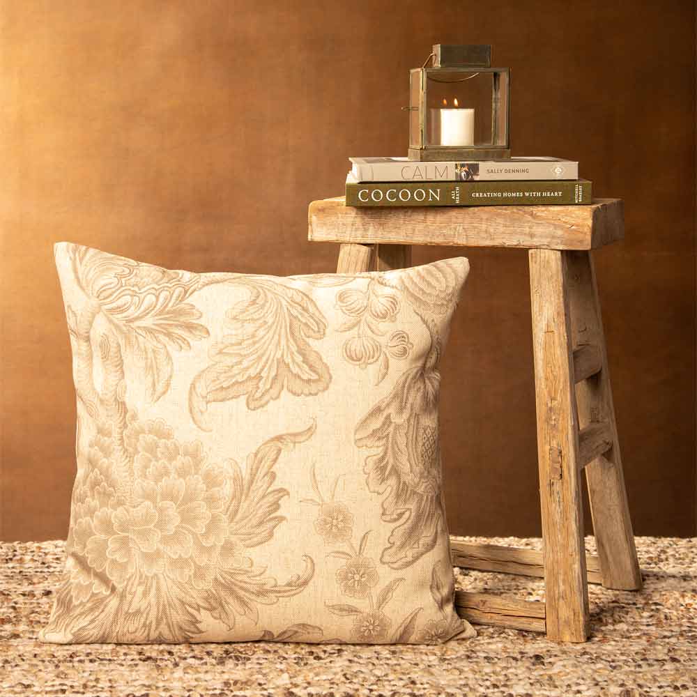 Decorative pillow with floral patterns on a textured surface, with a wooden stool and books in the background.