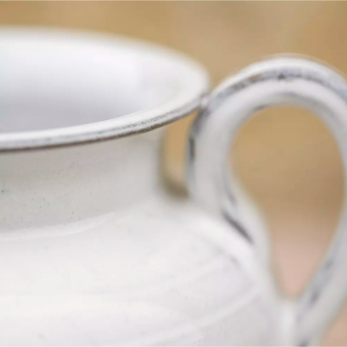 Carla White Glazed Jug – detail of the loop handle and rounded body showing glossy ceramic finish on a textured stone and wood background