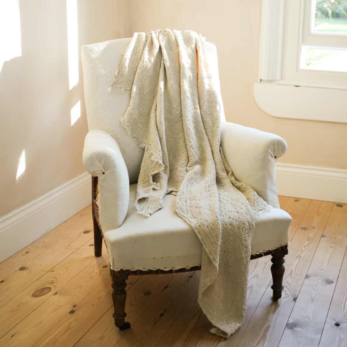 Antique white cotton throw – styled on armchair with relaxed waffle weave and soft frayed trim