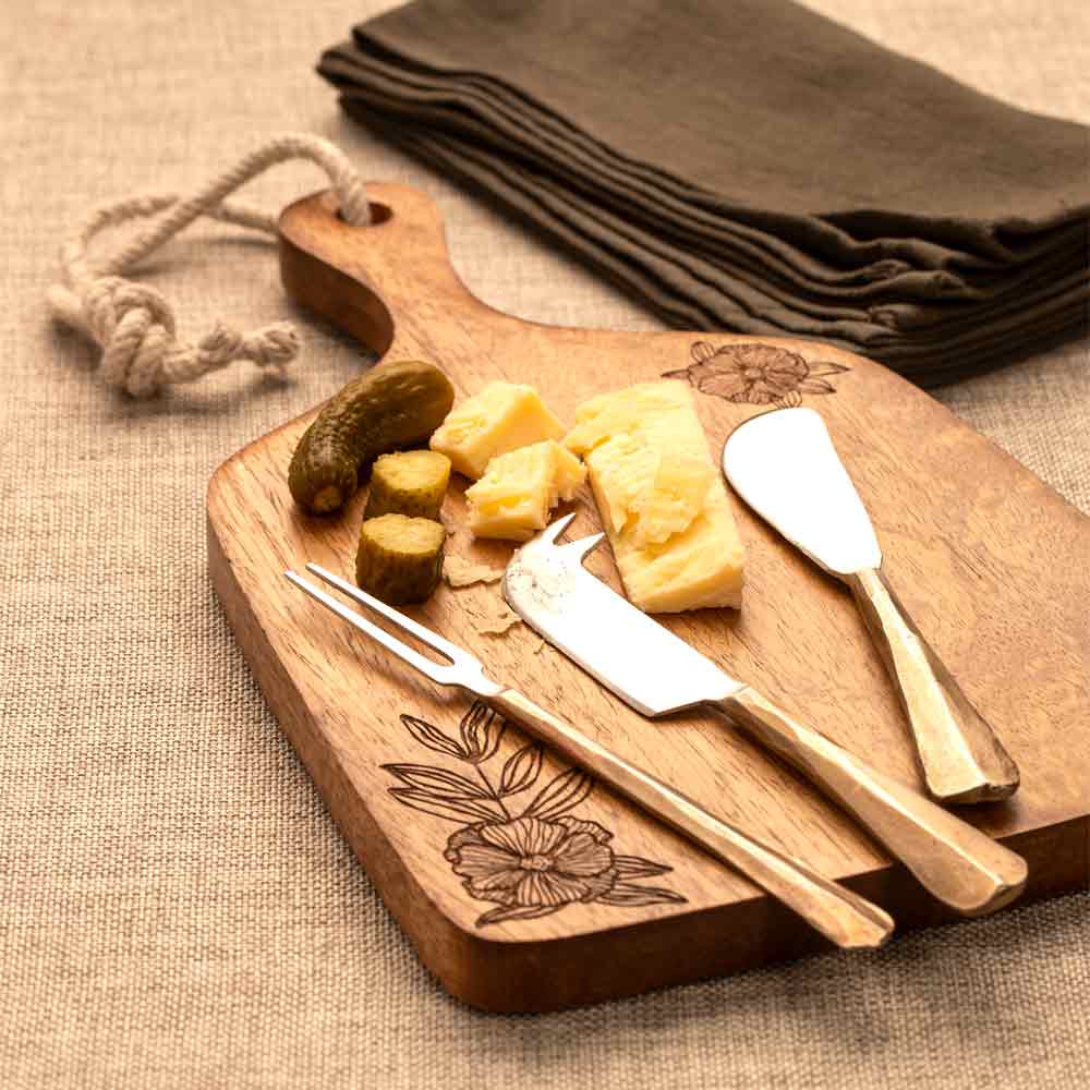 Wooden cutting board with cheese, and Pickle utensils on a textured surface