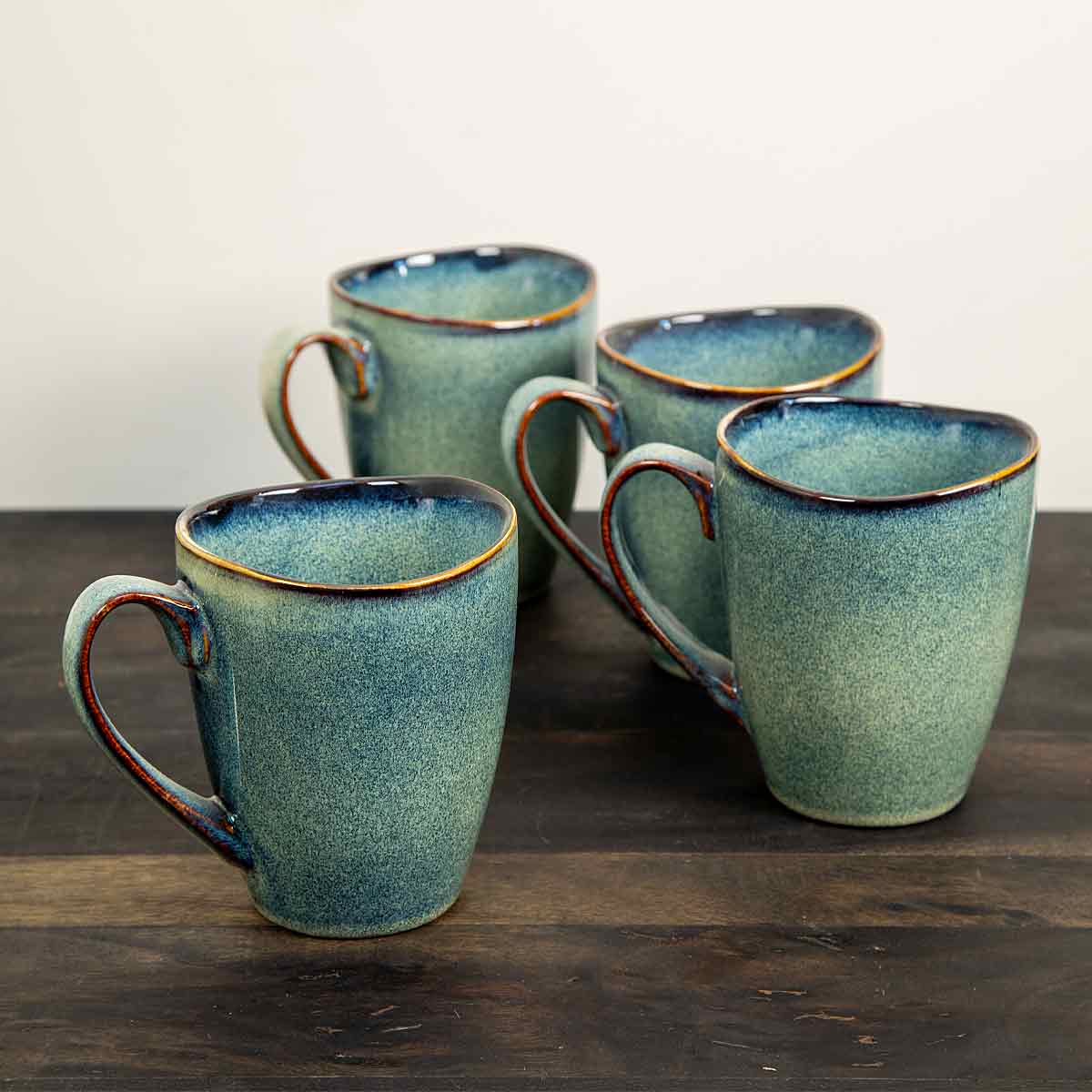 Four reactive glaze cornflower blue stoneware mugs displayed on a wooden surface