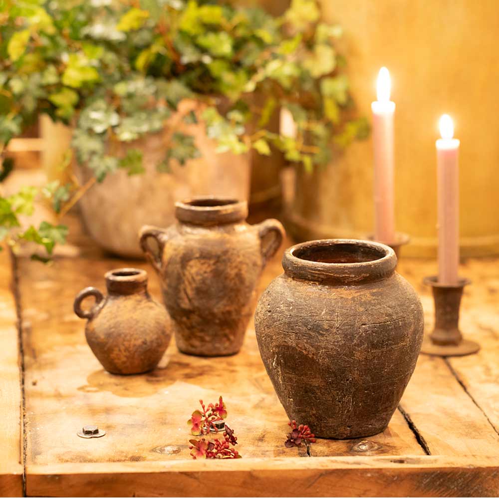 Vintage style Daiane Brown Terracotta vases on a wooden surface with candles and plants in the background