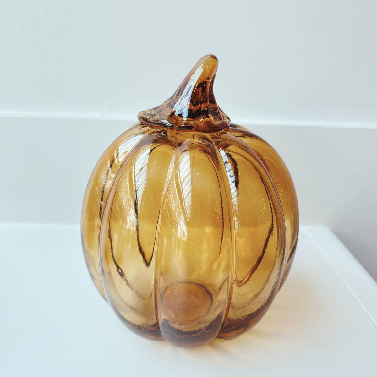Glass pumpkin ornament on a white surface with a light gray background - Dark Amber