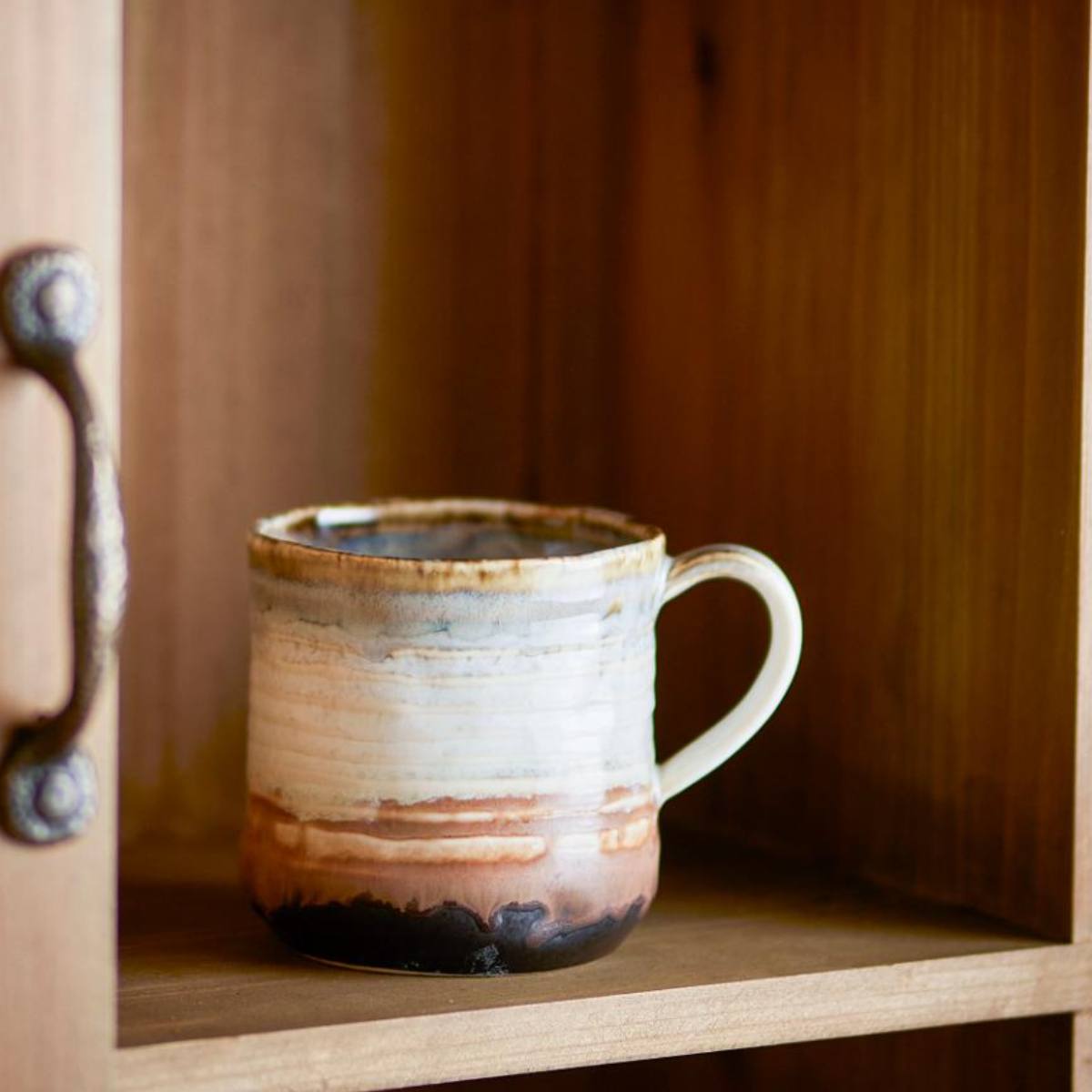 Ceramic Deana mug with brown and white glaze on a wooden shelf