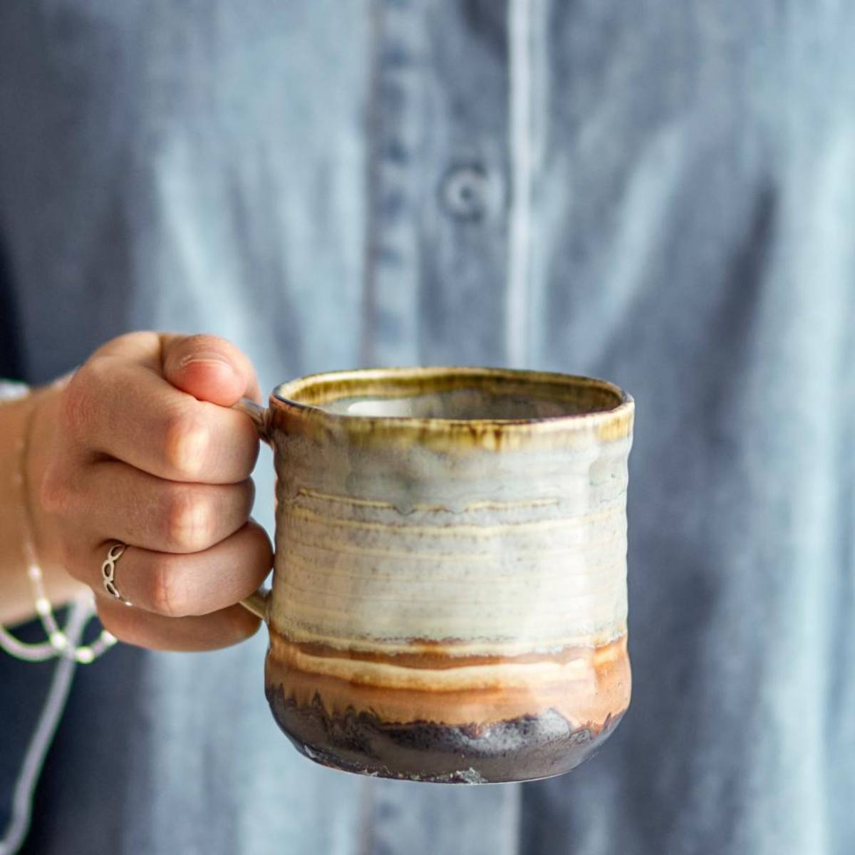 Hand holding a ceramic mug with a textured surface against a blurred background