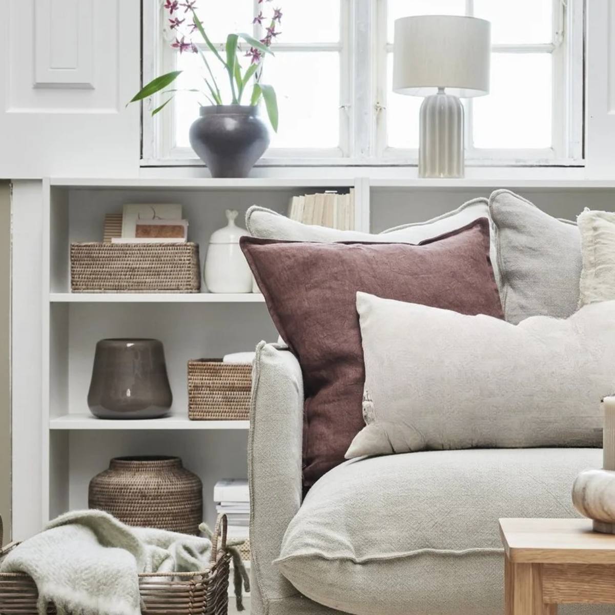 Cosy living room with a beige sofa, decorative pillows, including the Efina Rose Tan Linen Square Cushion, and a bookshelf.