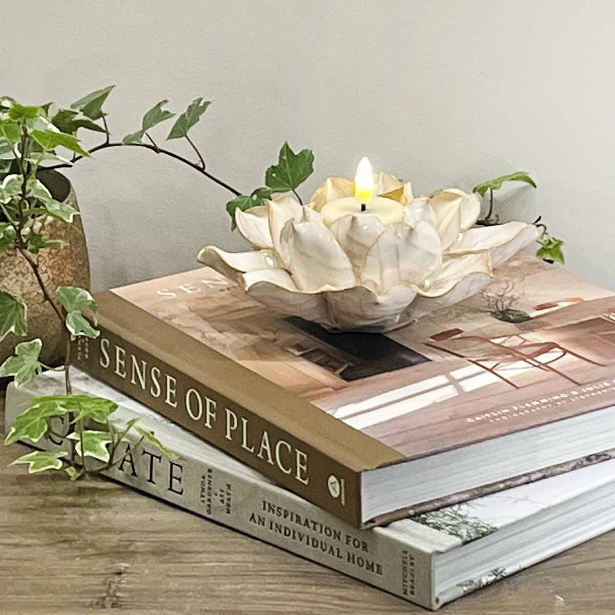 Eira Stoneware Tealight Holder in natural tones with delicate petal details, placed on stacked interior design books with a glowing LED tealight candle.
