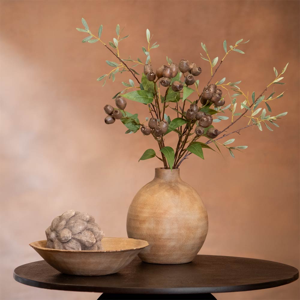 Decorative vase with branches and berries on a table against a brown background