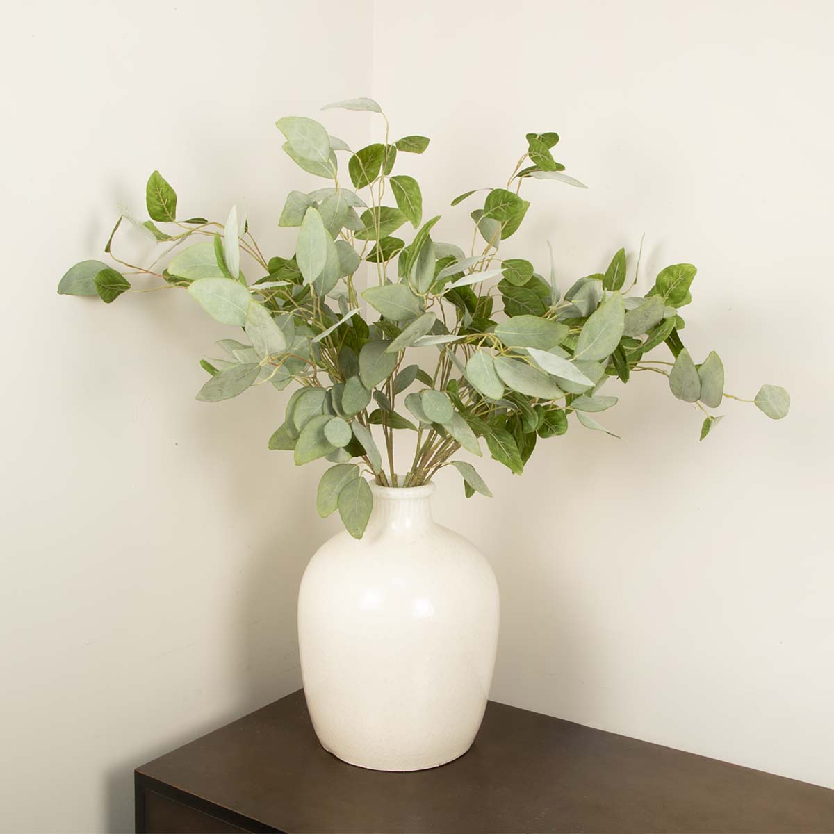 White vase with Faux Eucalyptus Silver Dollar Green leaves on a dark surface against a light background