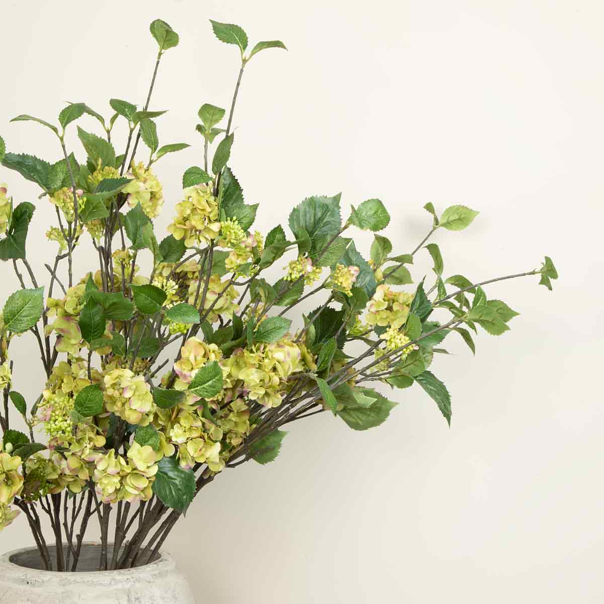 An arrangement of artificial green hydrangea sprays with multiple branches and green leaves in a ceramic vase