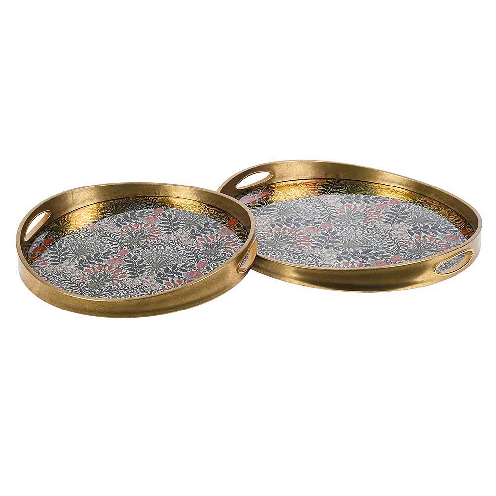 Two round brass serving trays with cutout handles, featuring a detailed floral and leaf pattern in gray, pink, and gold on the interior, set against a plain white background.