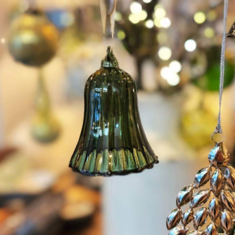 Decorative Glosille Green Glass Ornament Bell and silver tree ornament hanging against a blurred festive background.