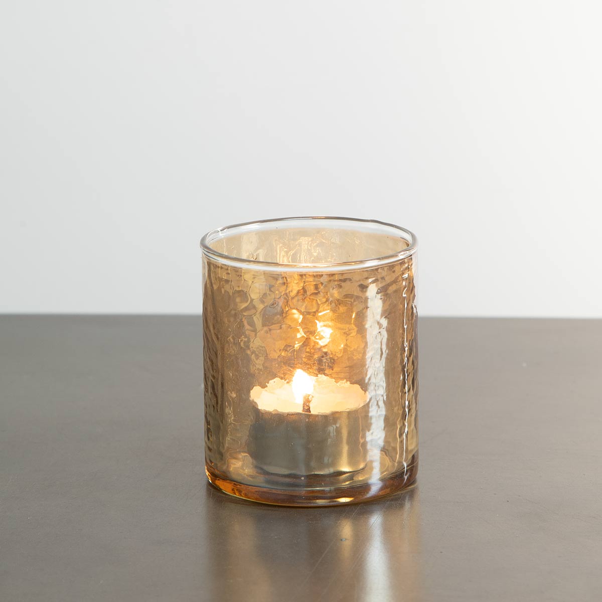 Hammered gold glass tealight holder with textured surface and soft candle glow