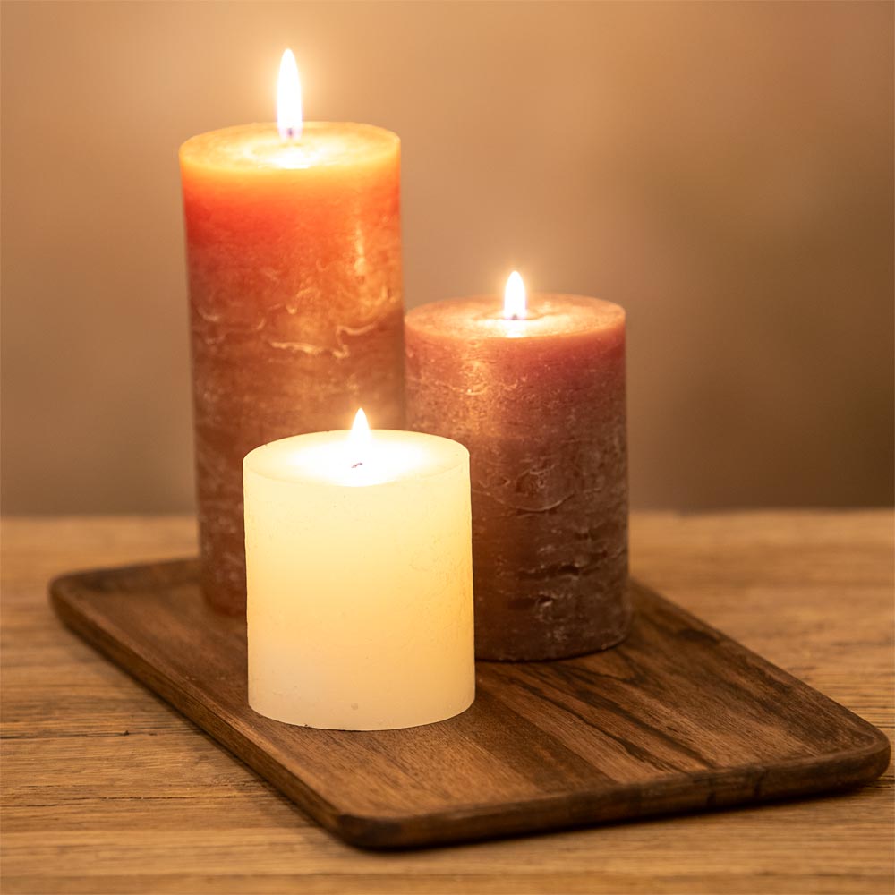 Three candles of different colors on a wooden tray with a warm background