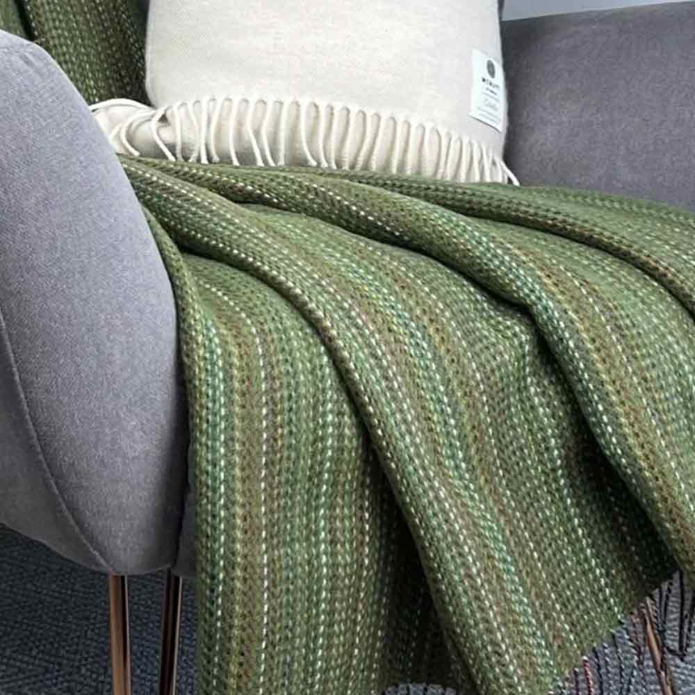 Heritage Meadow Green Tweed - Pure Merino Wool Throw - McNutt of Donegal draped over a grey chair with a white pillow.