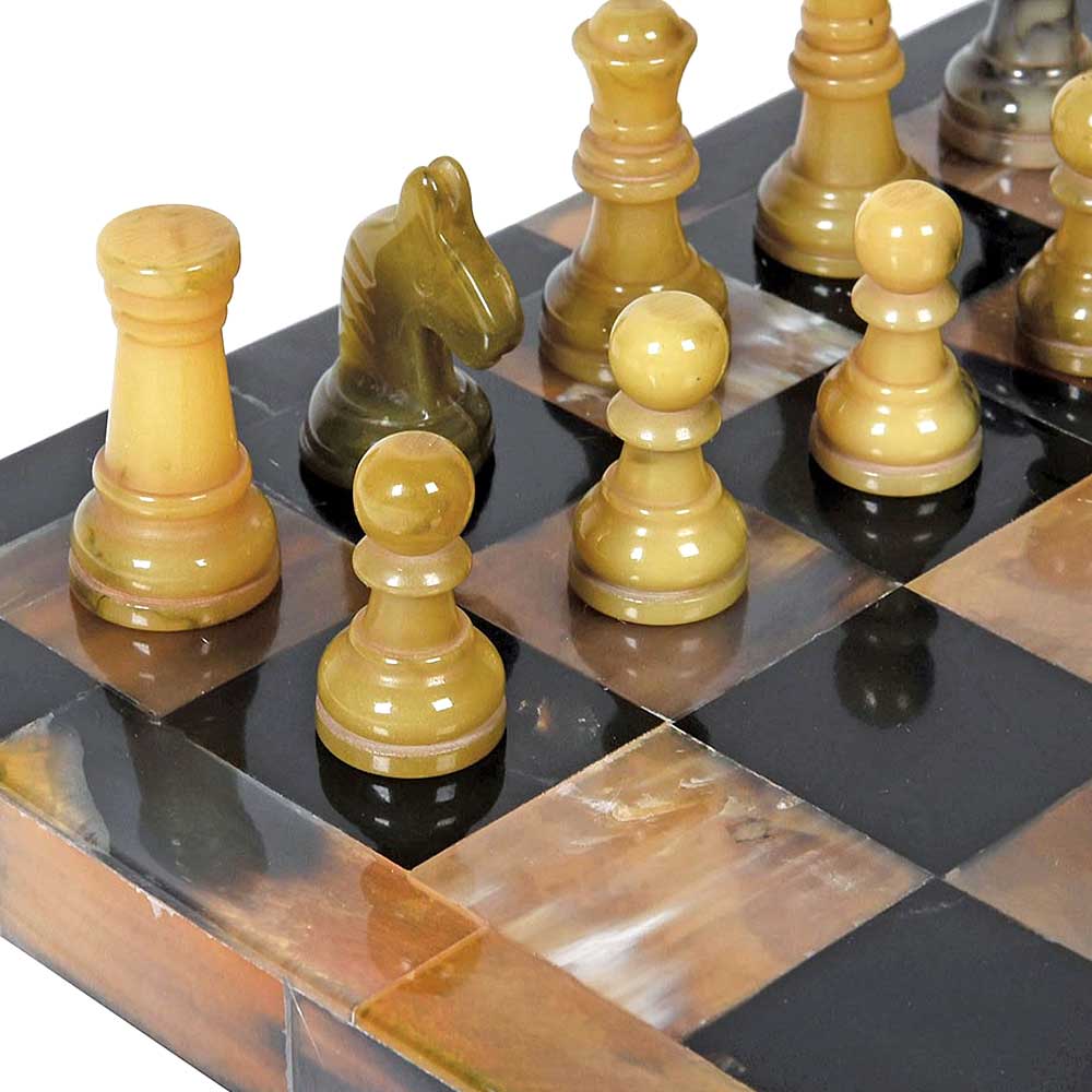 A close-up of a polished horn chess set on a checkered board, featuring light tan and green pieces with glossy, reflective surfaces.