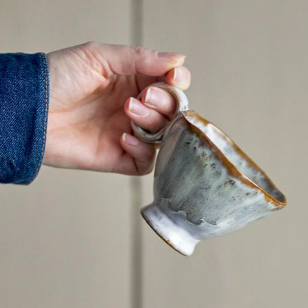 Hand holding a handmade Imogen cup with grey-green reactive glaze with a neutral background