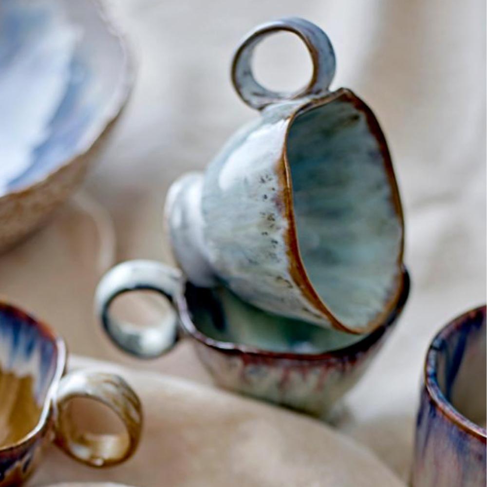 Handmade Imogen cup with grey-green reactive glaze stacked on other cups on a table