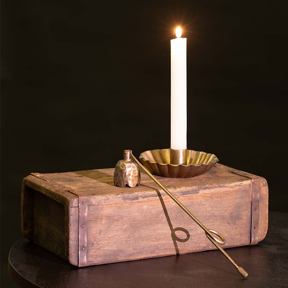 view of Ingrid Light Gold Candle Snuffer made from iron with bell design on rustic brick mould against a dark Background