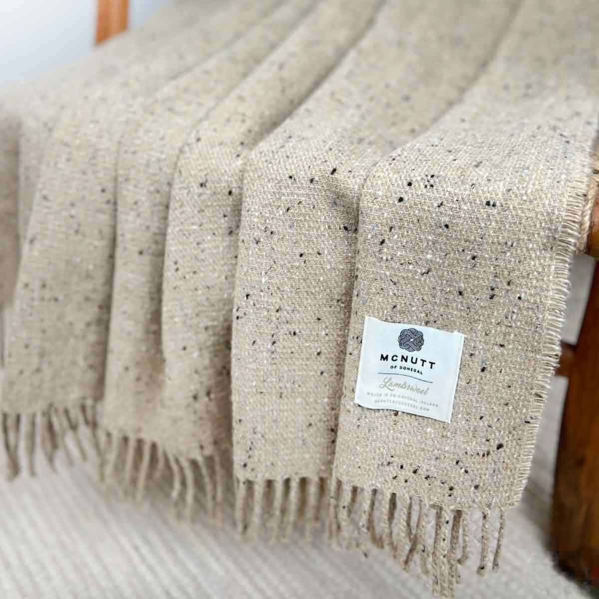McNutt Inishkeel Oatmeal Donegal Lambswool Tweed Throw draped on rustic wooden chair