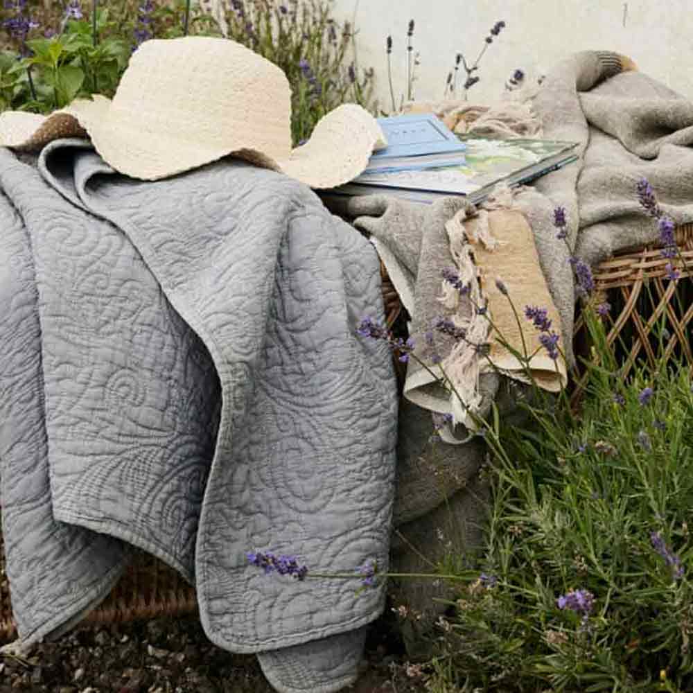 Isabelle Quilted Throw – lightweight grey throw showing stitched texture - draped on garden rattan seating with summer hat