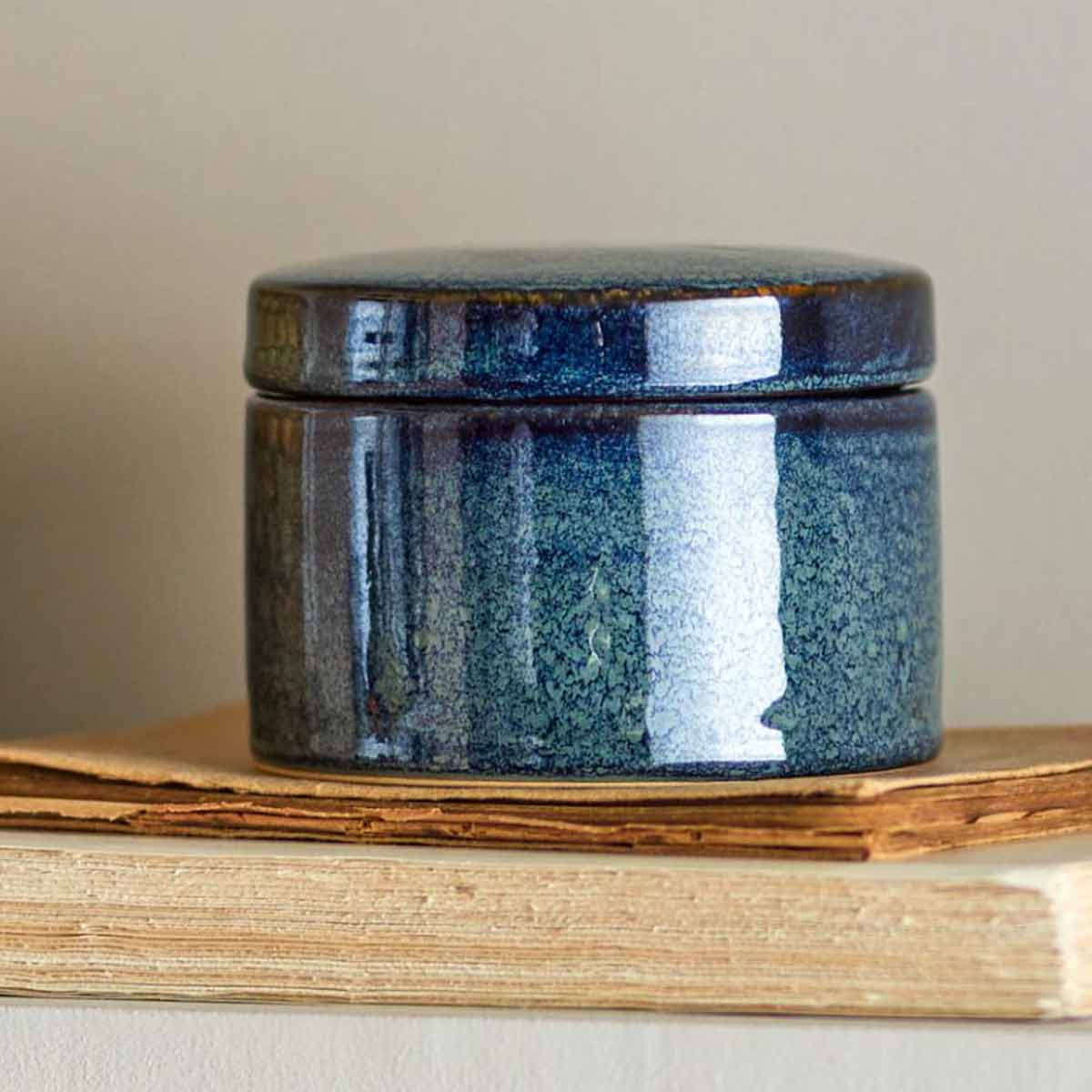 Khai Jar, a deep blue stoneware storage jar with a glazed finish and lid - displayed on rustic books.
