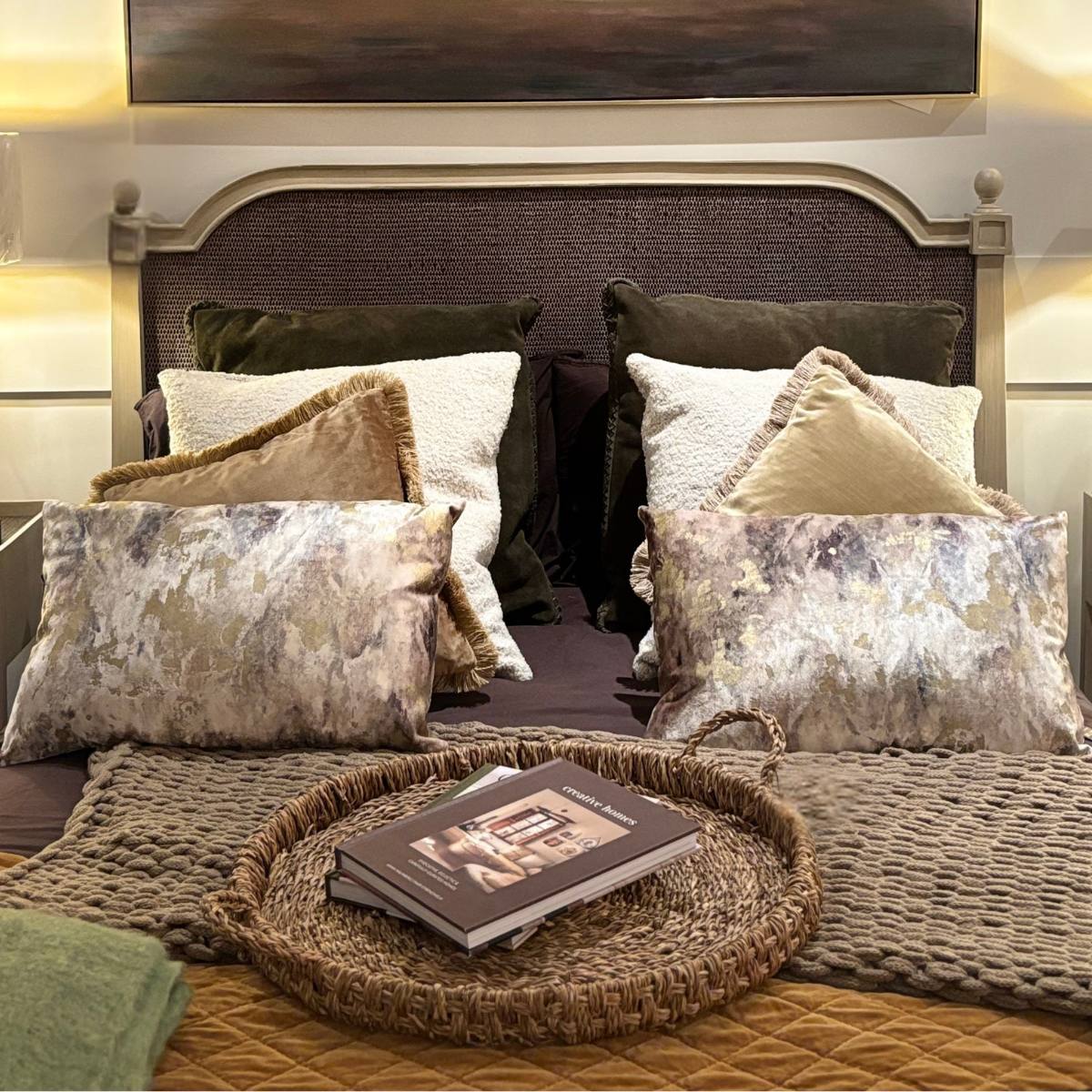 Decorative pillows on a bed with a Large Seagrass Serving Tray and book in a bedroom setting.