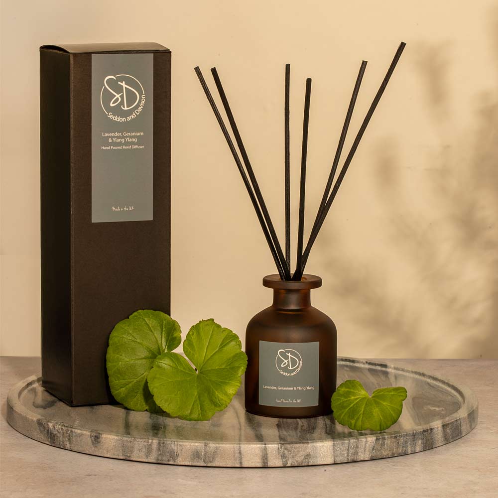 Lavender and Geranium Diffuser bottle with sticks and packaging on a marble surface