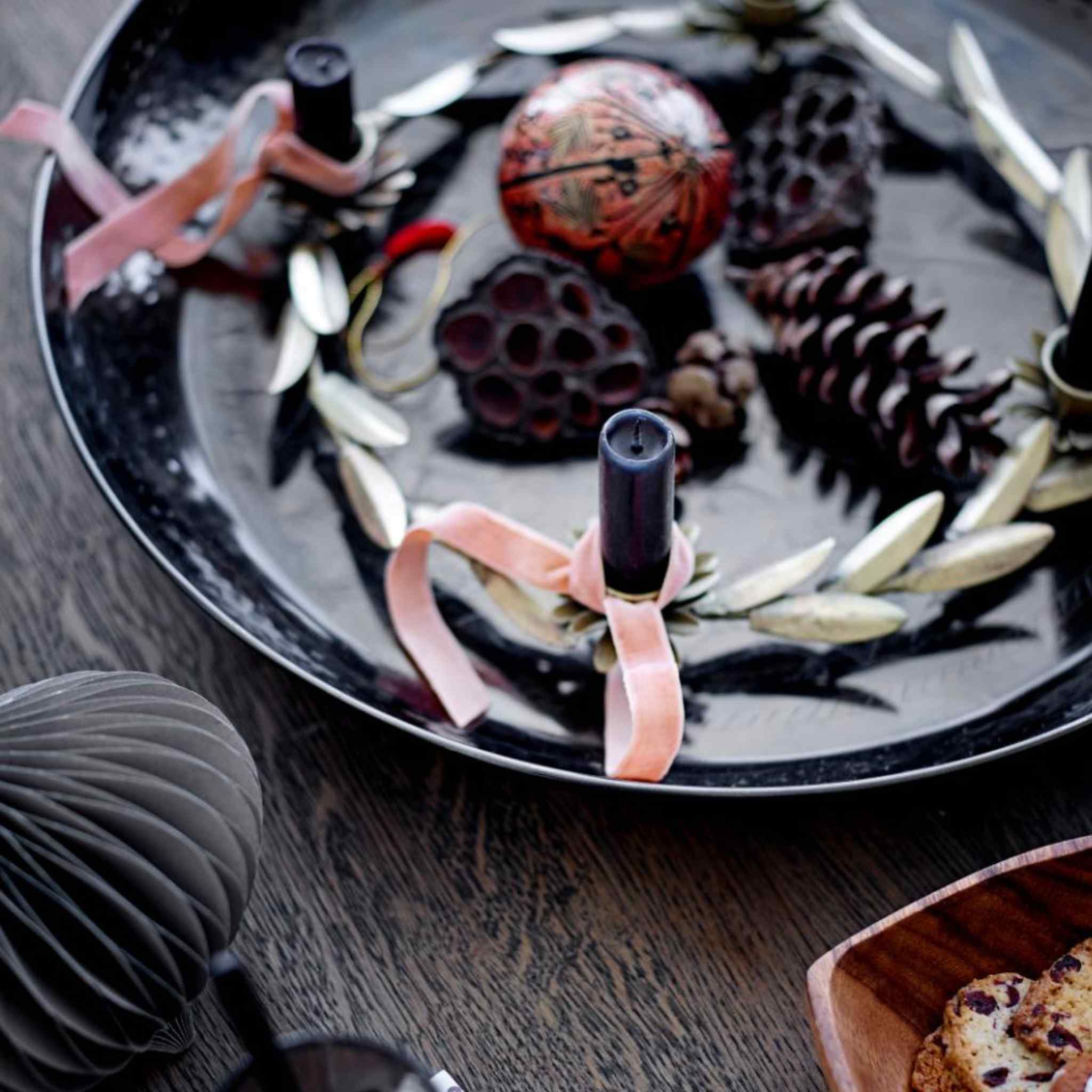 Leonetta leaf metal advent candle holder with four spaces for candles, decorated with pine cones, leaves, and ribbons on a wooden surface.
