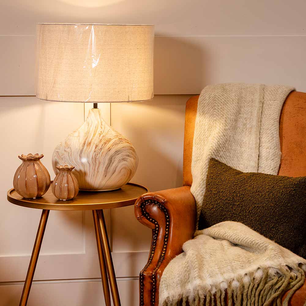 Marble effect lamp with linen shade on side table styled with leather armchair and soft furnishings
