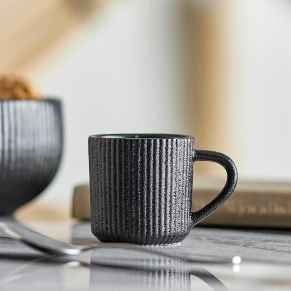 Neri Stoneware Espresso Cup in Black on a reflective surface with a blurred background