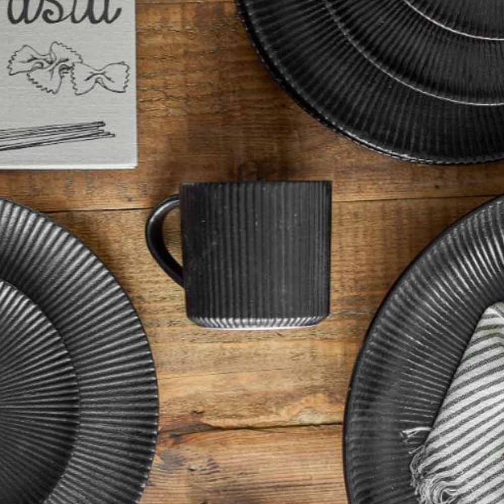 Neri Ribbed Stoneware Mug in Black shown with plates on a wooden surface.