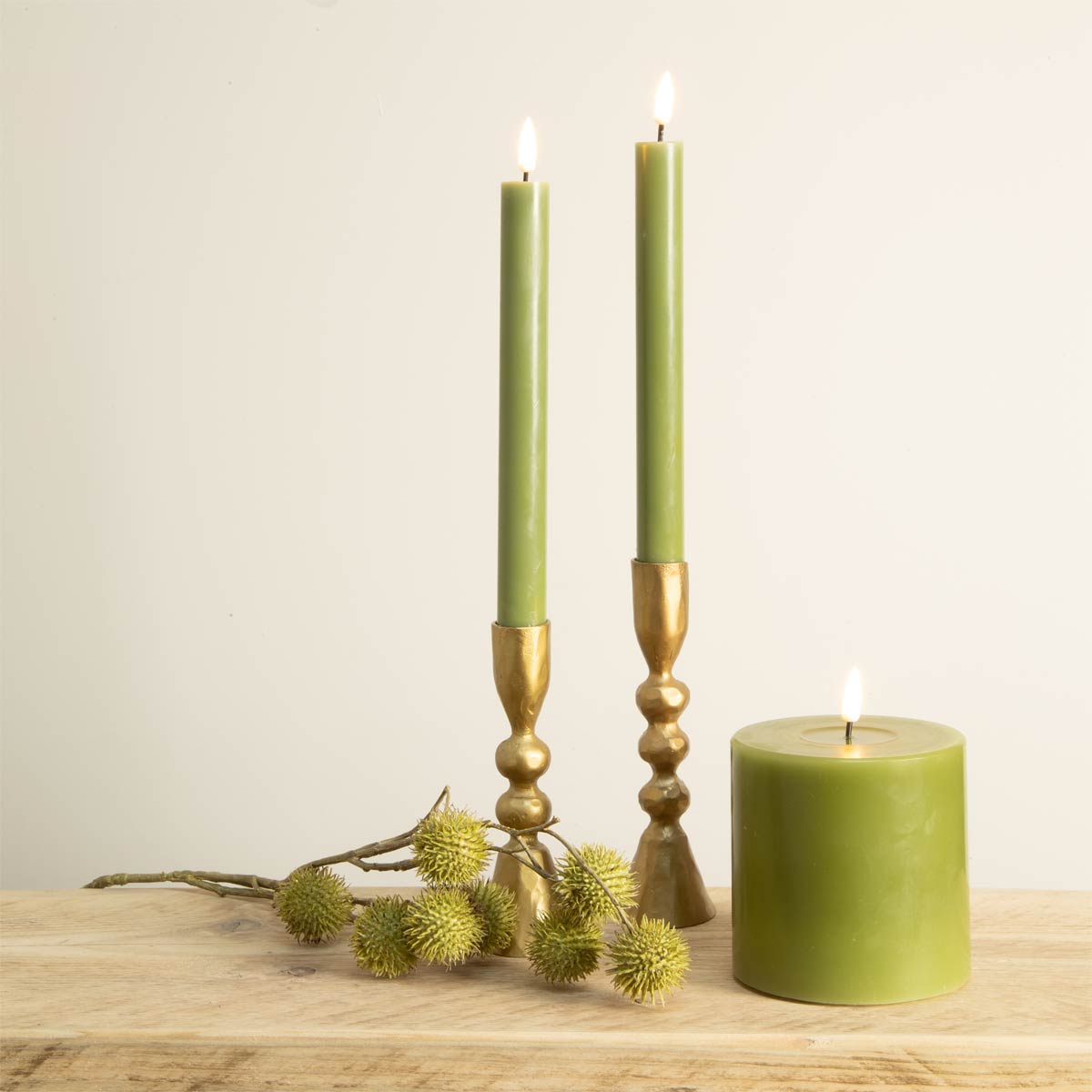 Olive green LED dinner candles in gold holders and wide pillar candle – styled for indoor decor
