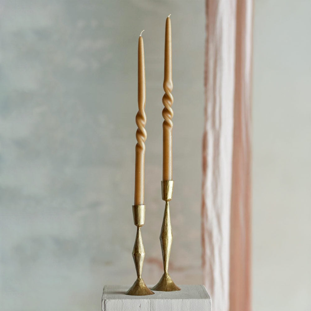 Two gold candlesticks featuring Twist Dinner Candles in Caramel on a grey background